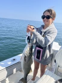 A young angler proudly displaying a striped bass while fishing on a boat, enjoying a sunny day on the water.
