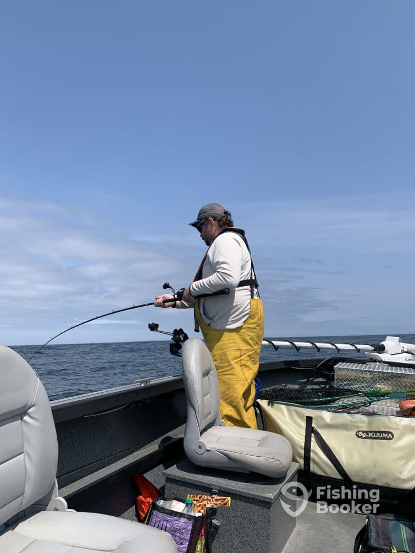 An angler in yellow fishing gear is actively reeling in a catch from a boat, surrounded by a scenic ocean backdrop.