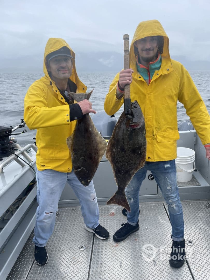 Two anglers proudly displaying their catch of large Halibut while fishing on a boat in overcast weather.