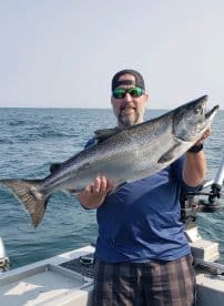 An angler proudly displaying a large Chinook Salmon while fishing on a boat in open waters.