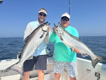 Two anglers proudly displaying their large Silver Salmon while fishing offshore, showcasing a successful day on the water.