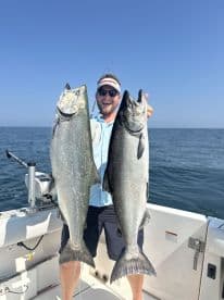 Angler proudly displaying two large Salmon while fishing on a sunny day at sea.