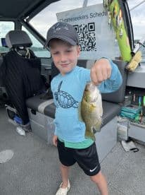 A young angler proudly displaying a freshly caught fish inside a fishing boat, showcasing a fun day on the water.