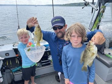 A proud moment for two young anglers holding their catches of Largemouth Bass while fishing on a boat.