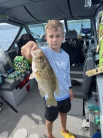 A young angler proudly displaying a large Largemouth Bass while fishing on a boat, showcasing a fun day on the water.