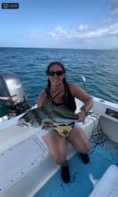 An angler proudly displaying a large fish while aboard a boat in open water, showcasing a successful fishing trip.