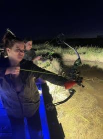 Two anglers engaged in bowfishing at night, showcasing the excitement of fishing in a unique environment.