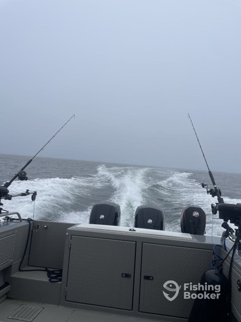View from the helm of a fishing boat, showcasing the dual engines and fishing rods as it navigates through a foggy sea.