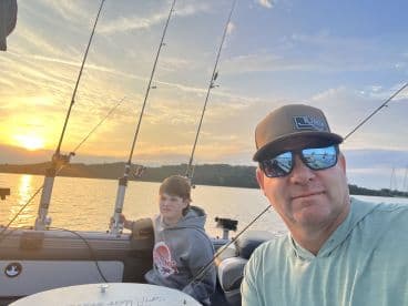A father and son enjoying a peaceful evening on the water, with fishing rods ready as the sun sets behind them.
