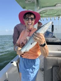 An excited angler proudly displaying a caught shark while aboard a fishing boat, enjoying a sunny day on the water.