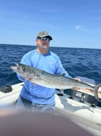 An angler proudly displaying a large King Mackerel while fishing offshore, showcasing a successful day on the water.