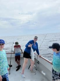A proud angler displaying a large fish on a fishing charter, surrounded by excited kids on a boat in open waters.