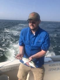 Angler holding a Spanish Mackerel while fishing offshore, showcasing a successful catch during a charter trip.