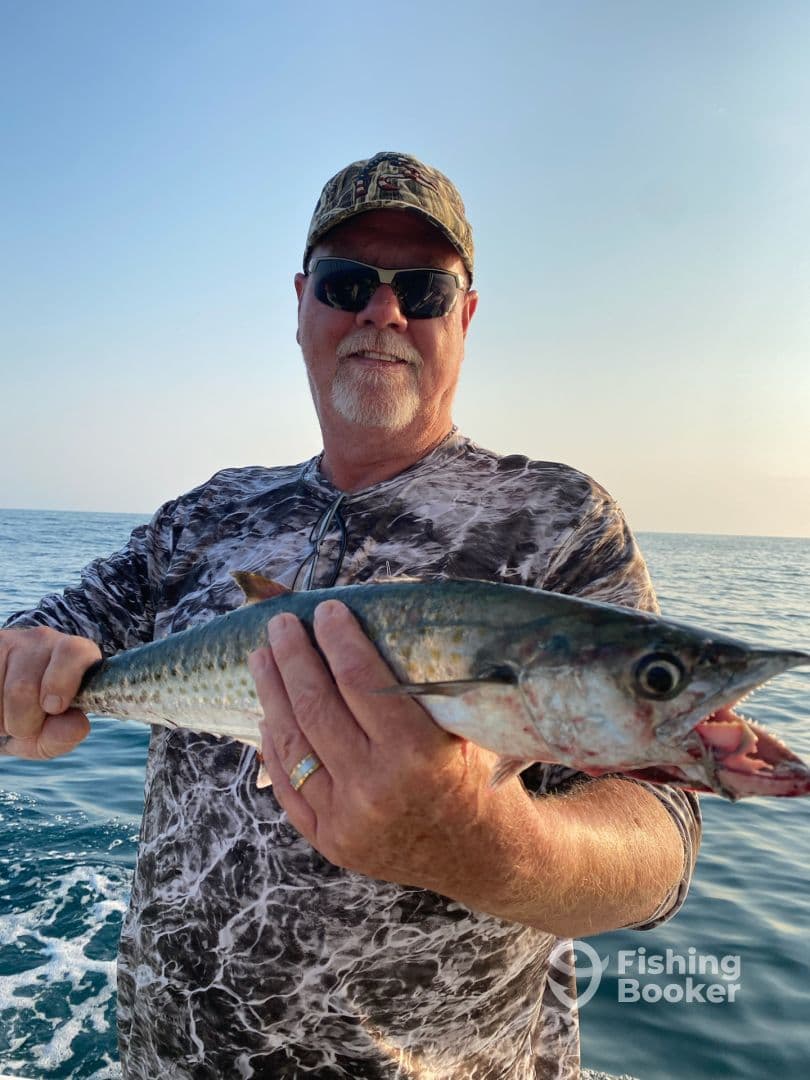 An angler proudly displaying a large Spanish Mackerel while fishing in open waters.