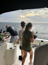 A group of young anglers enjoying a fishing trip on a boat, with one person preparing bait while the others are engaged in fishing activities against a scenic ocean backdrop.