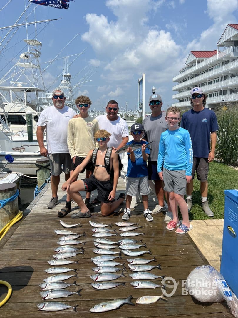 A group of anglers, including children, proudly display their catch of fish on a dock after a successful fishing trip.