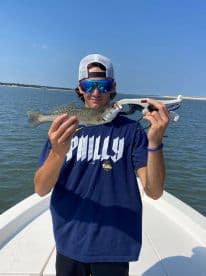 Young angler proudly displaying a Speckled Trout while fishing from a boat in a coastal waterway.