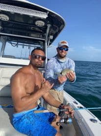 Two anglers enjoying a day on the water, with one proudly displaying a caught fish while the other poses with a fishing rod on a modern boat.