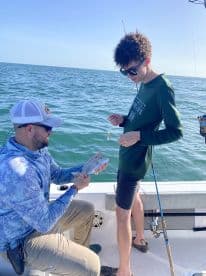 A young angler is engaged in fishing on a boat, receiving guidance while holding a freshly caught fish, showcasing a hands-on fishing experience.