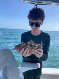 A young angler proudly displaying a colorful Grouper while fishing on a sunny day in clear waters.