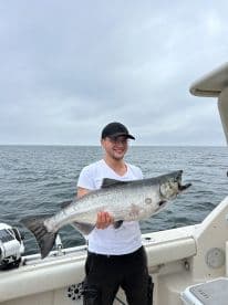 Angler proudly displaying a large Salmon while fishing offshore, showcasing a successful day on the water.