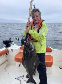 An angler proudly displaying a large Halibut while fishing on a boat in open waters.