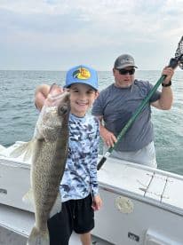 A young angler proudly displays a Walleye while fishing on a boat, accompanied by an adult. The scene captures a joyful moment on the water.