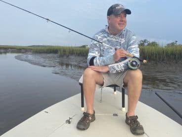 An angler enjoying a peaceful moment while fly fishing from a skiff in a scenic marsh environment.