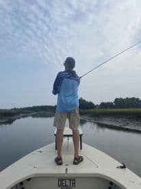 An angler casting a line from the bow of a fishing boat in a serene marsh environment, showcasing the excitement of fishing.