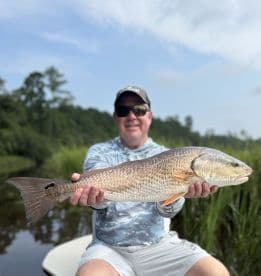 An angler proudly displaying a large Redfish while fishing in a scenic coastal environment.