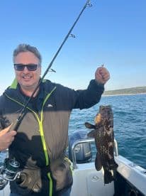 An angler proudly displaying a large Grouper while fishing from a boat, showcasing a successful day on the water.