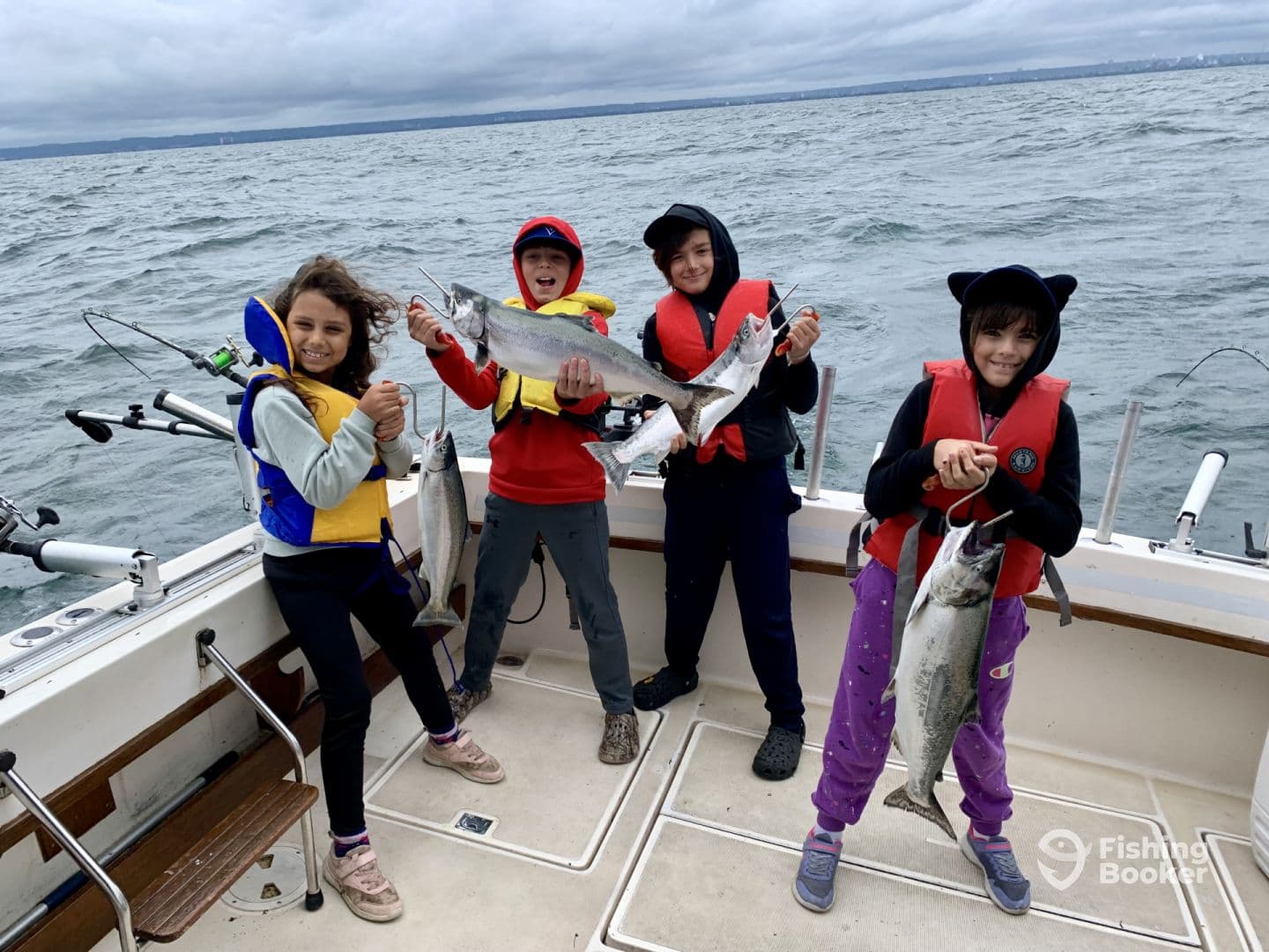 Four young anglers proudly displaying their catches of salmon while fishing on a boat in a coastal environment.