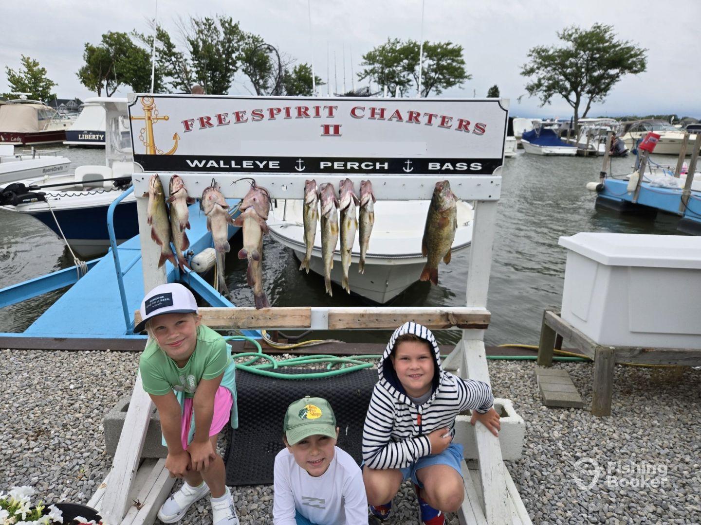 Three young anglers posing in front of a catch board displaying Walleye and Bass after a successful fishing trip with Freespirit Charters.