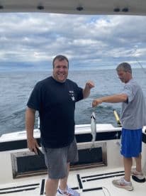 Two anglers on a fishing charter proudly displaying their catch on a boat, with a scenic ocean backdrop.