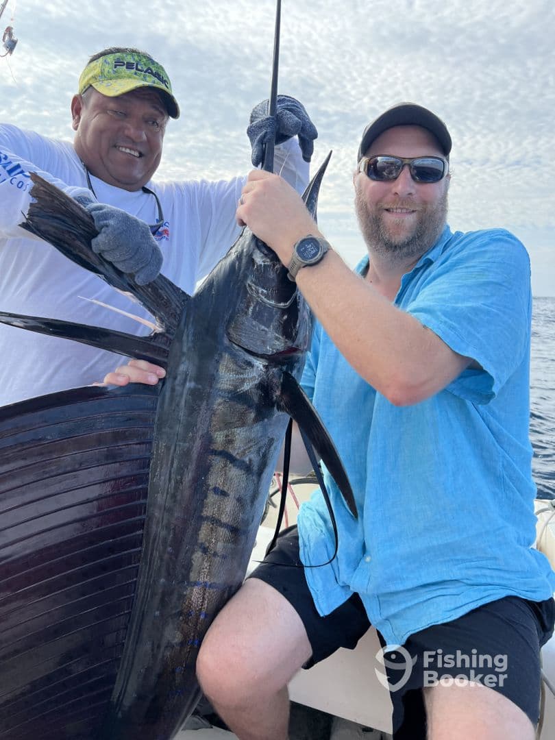 Two anglers proudly displaying a large Sailfish while fishing offshore, showcasing a successful deep-sea fishing experience.