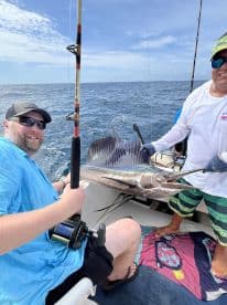 Two anglers proudly displaying a large Sailfish while fishing offshore, showcasing the excitement of deep-sea fishing.