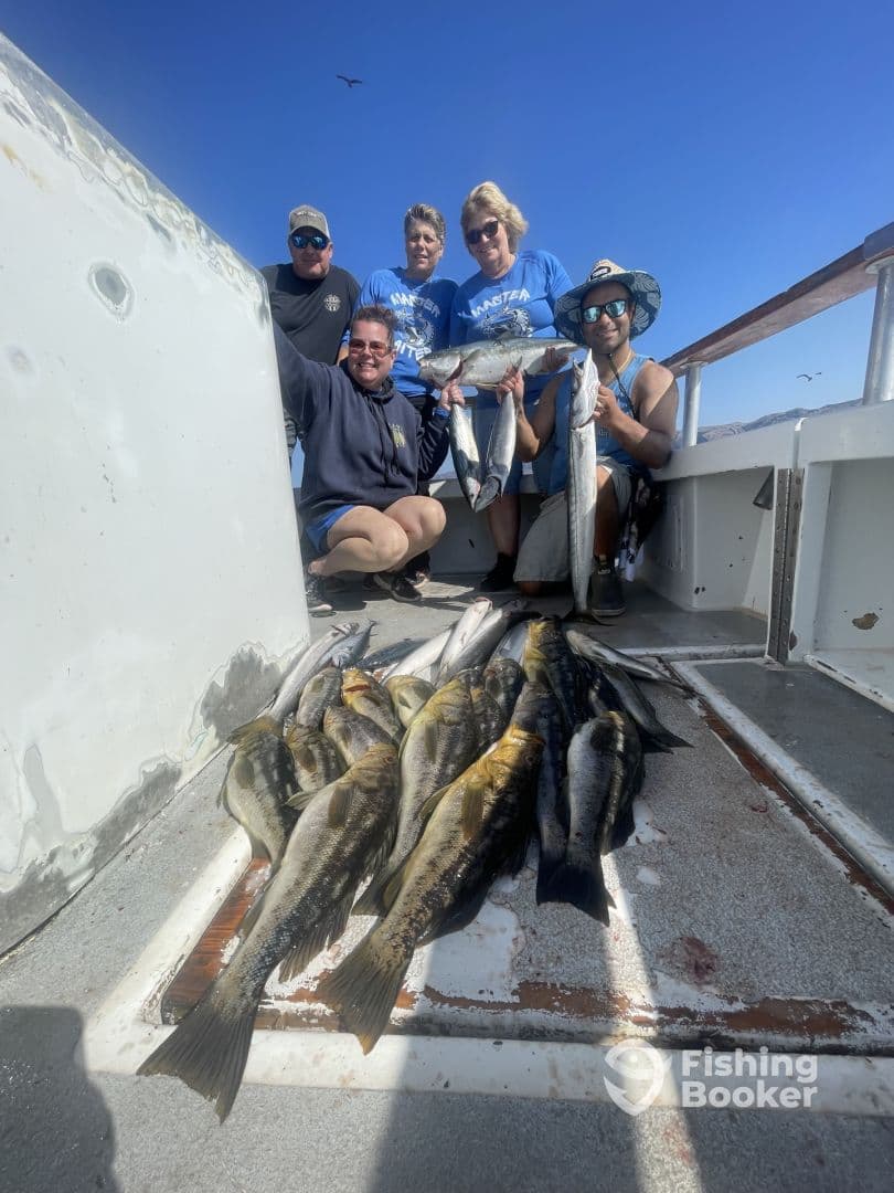 A group of anglers proudly displaying their catch of multiple fish, including large bass, aboard a fishing boat in a sunny environment.