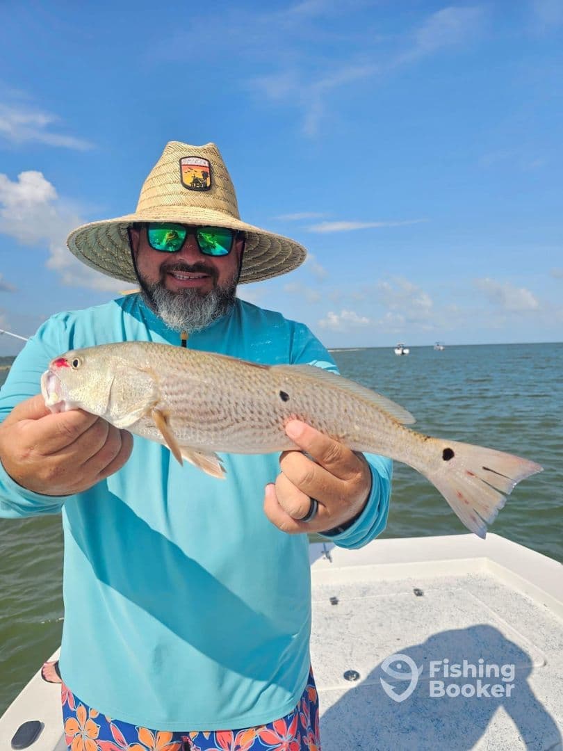 An angler proudly displaying a Redfish while fishing on a sunny day in coastal waters.
