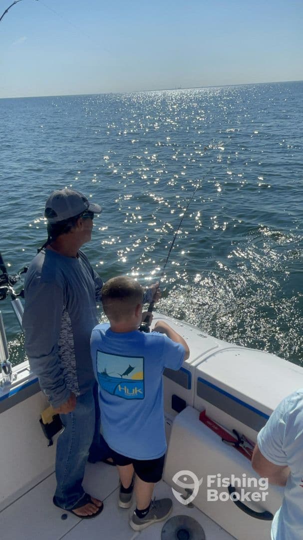 A young angler and an adult are actively fishing on a boat, with the sun reflecting off the water, creating a vibrant fishing atmosphere.