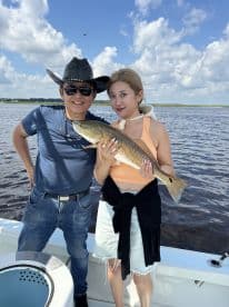 Two anglers proudly displaying a Redfish while enjoying a sunny day on the water.