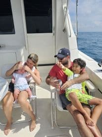A family enjoying their time on a boat, with a baby and a young boy playing while seated in the cabin area.