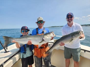 A family proudly displaying their catch of striped bass while enjoying a sunny day on the water.
