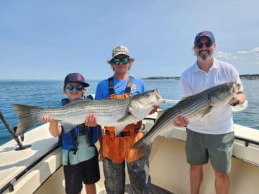 A young angler and his companion proudly displaying their catch of striped bass while enjoying a sunny day on the water.
