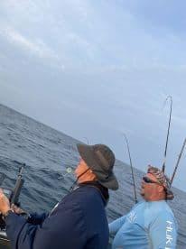 Two anglers actively fishing on a boat, focused on their lines in the open water, showcasing the excitement of a fishing trip.