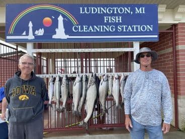 Two anglers proudly posing in front of a catch board displaying several Salmon at the Ludington, MI Fish Cleaning Station.