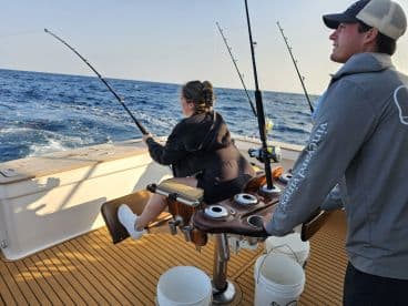 A woman actively reeling in a fish while fishing on a well-equipped boat, showcasing the excitement of deep-sea fishing.