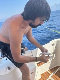 An angler on a boat carefully handling a small fish while fishing in open waters, showcasing the excitement of the catch.
