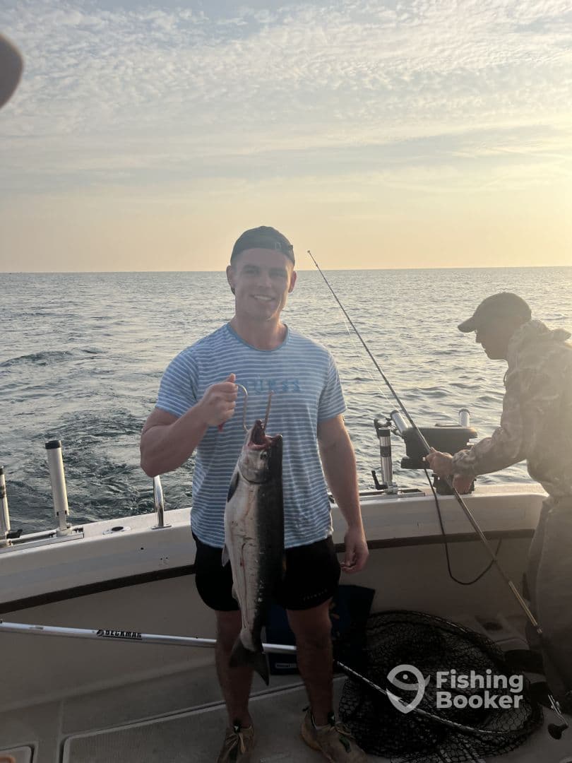 A young man proudly displaying a large Salmon while fishing on a boat during sunset.
