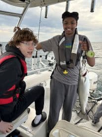 Two young anglers aboard a boat, with one proudly displaying a caught fish, showcasing a fun day of fishing.