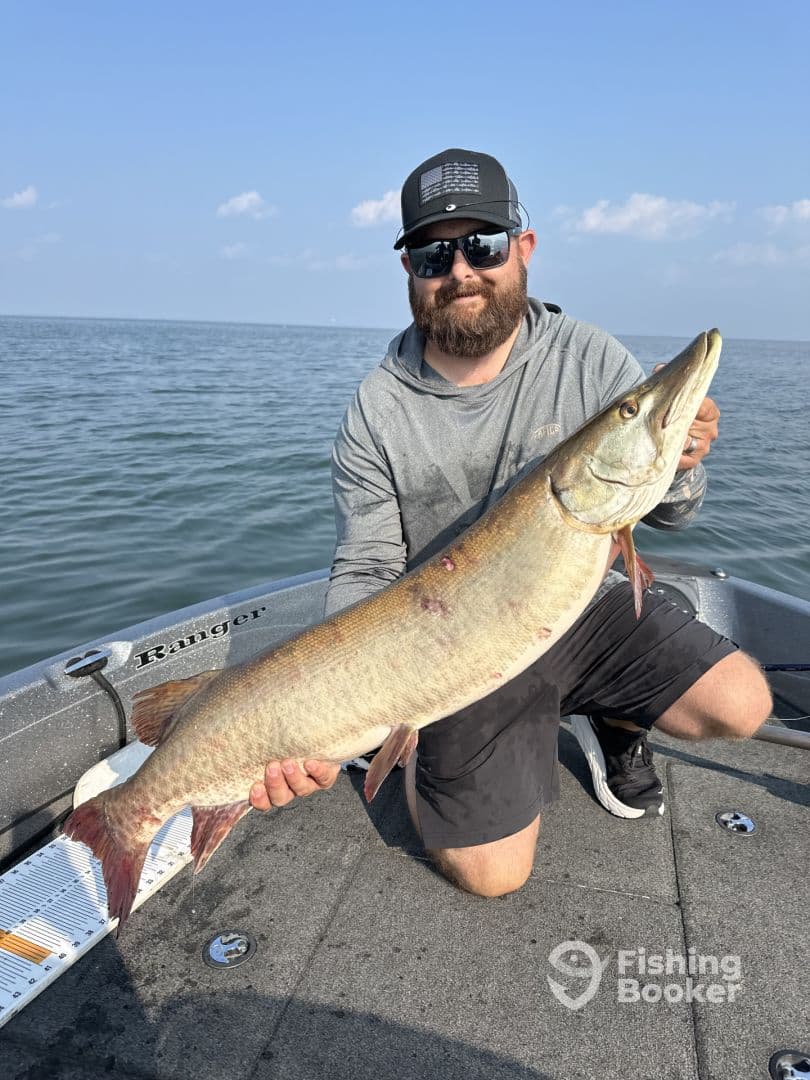 Angler proudly displaying a large Muskellunge while fishing on a boat in open water.